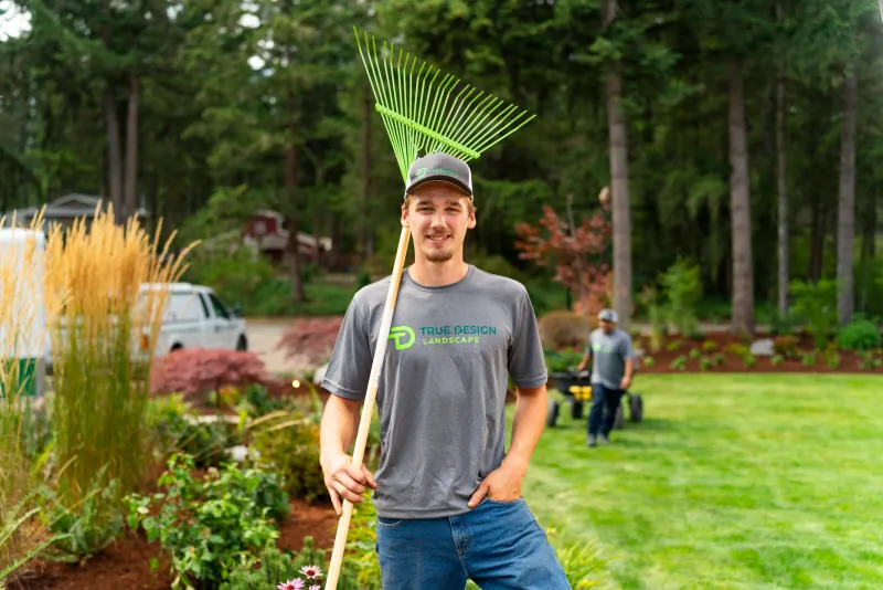 True Design Landscaping employee holding a rake in a landscaped residential yard